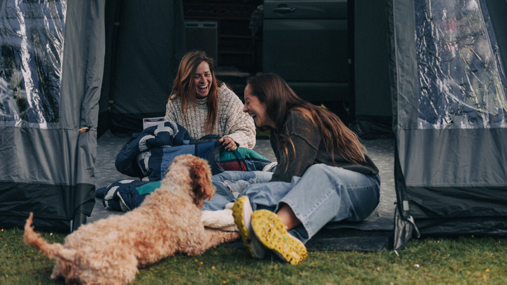 Two women in a Kampa tent laughing with their dog
