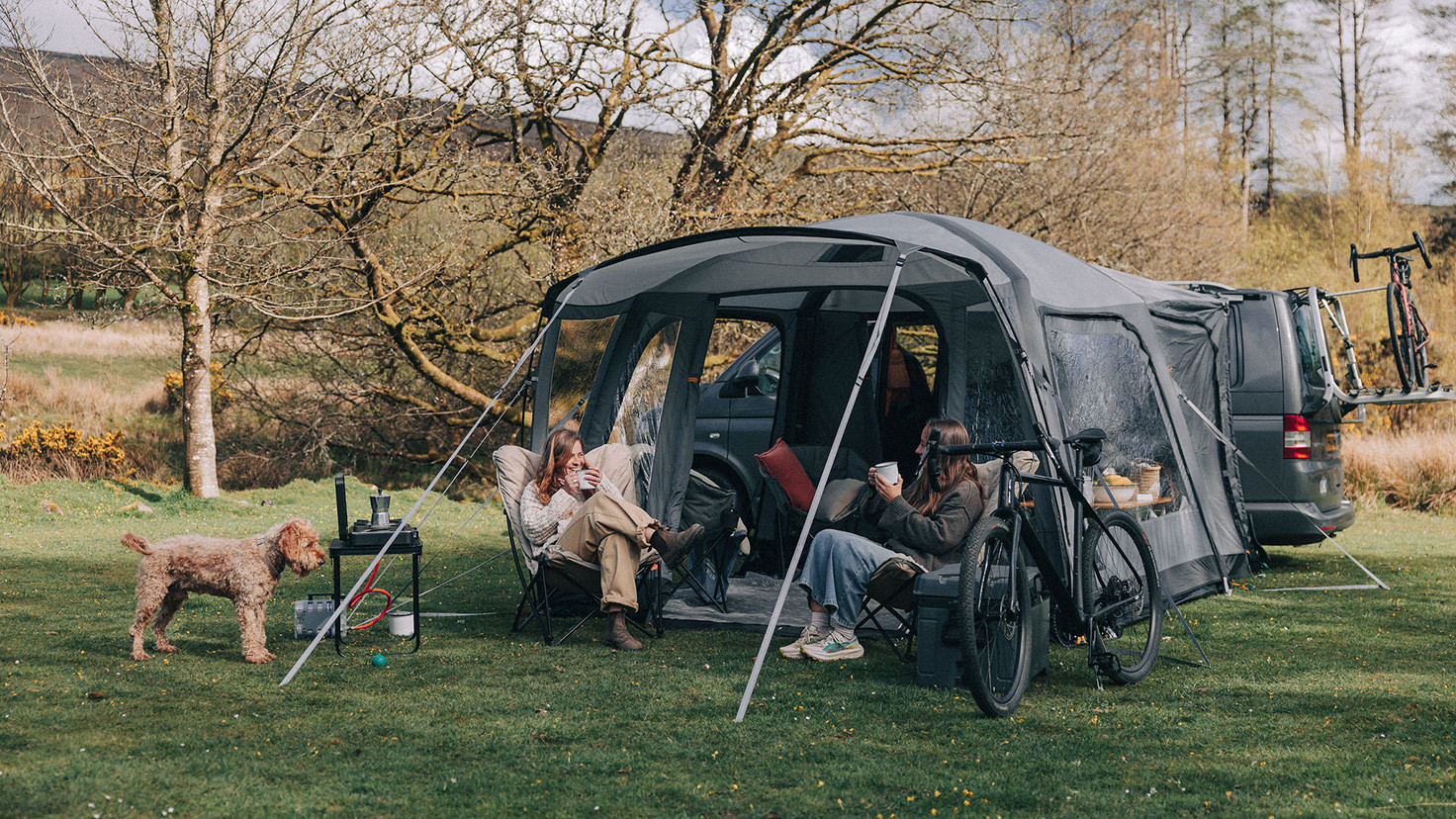 Two women enjoying a coffee in a Kampa drive-away tent with their Dog
