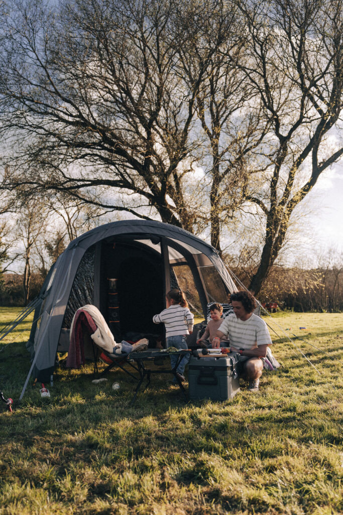 A man with his two young children preparing some food on a camping trip with their Kampa tent